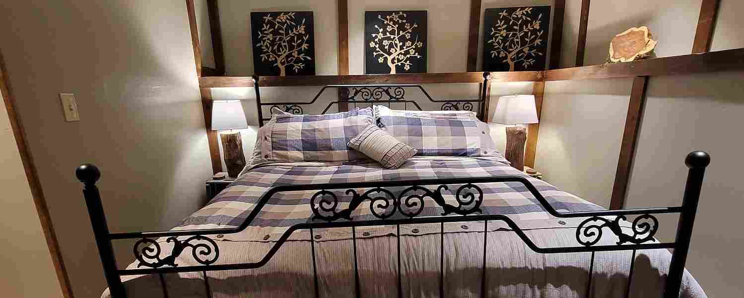 A king size iron bed topped with cozy plaid bedding & flanked with softly glowing table lamps awaits a restful night's sleep