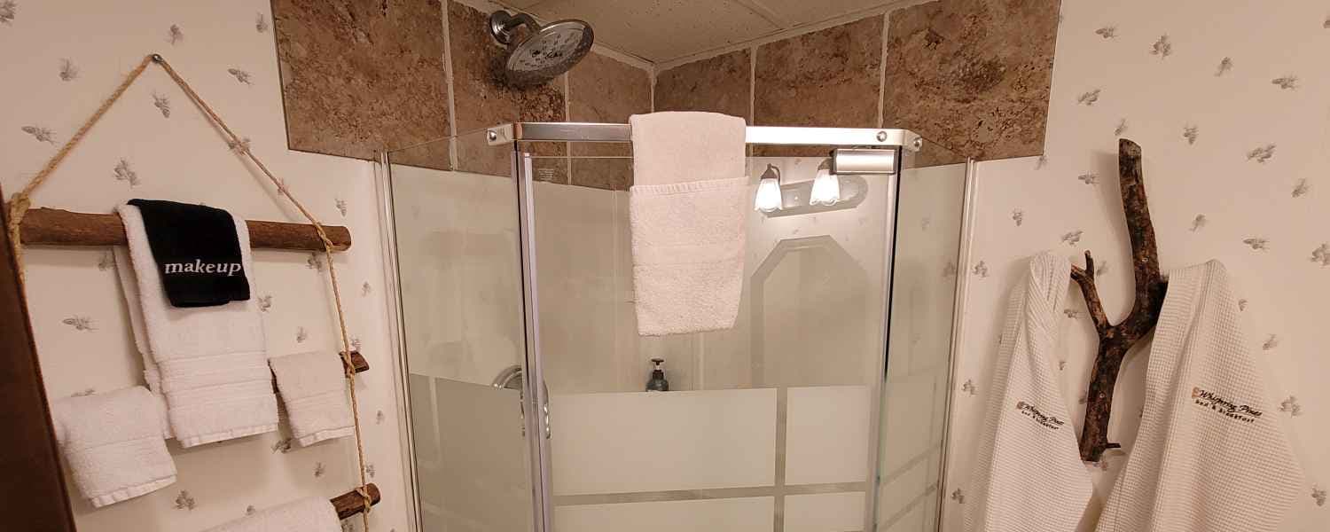 Tranquil bathroom in soothing neutral colors features a glass enclosed walk in shower and plush white towels hanging from natural wood branch hangers