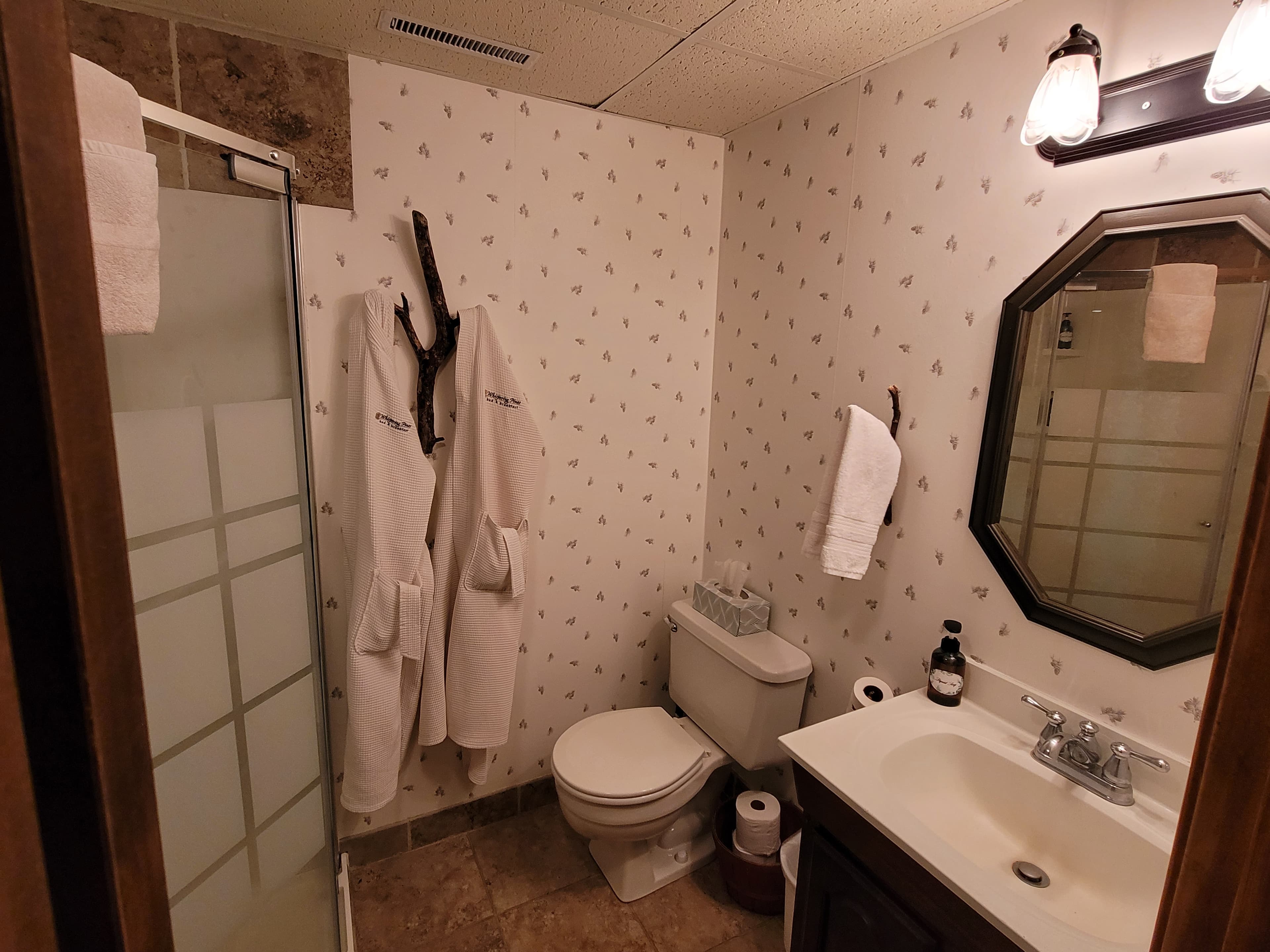 Pinecone wallpaper carries the subtle woodland theme into the bathroom with walk-in shower, toilet, and sink accented by natural branch towel holders