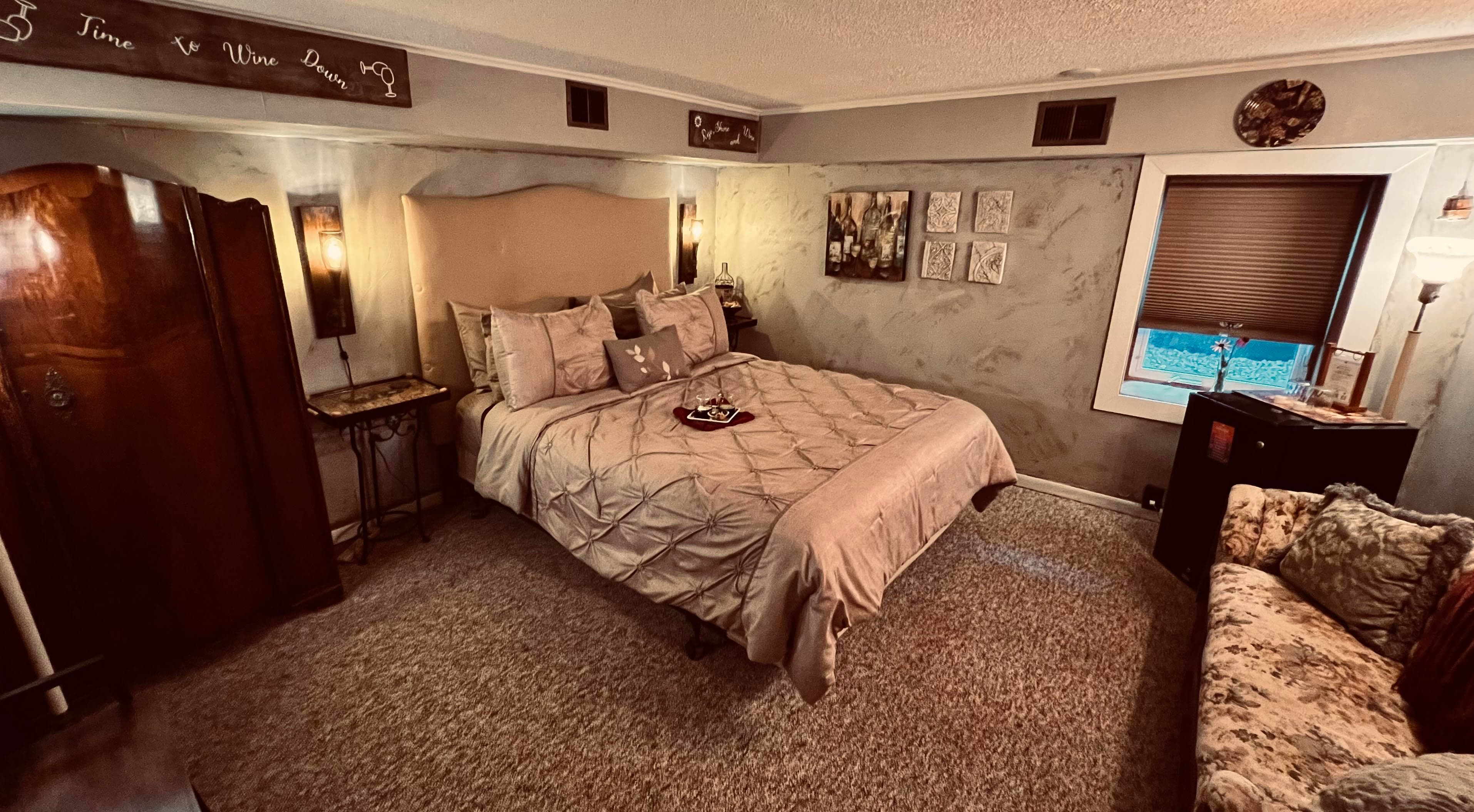 Cozy and secluded guestroom with antique armoire, queen bed with upholstered headboard, antique settee, and electric fireplace.