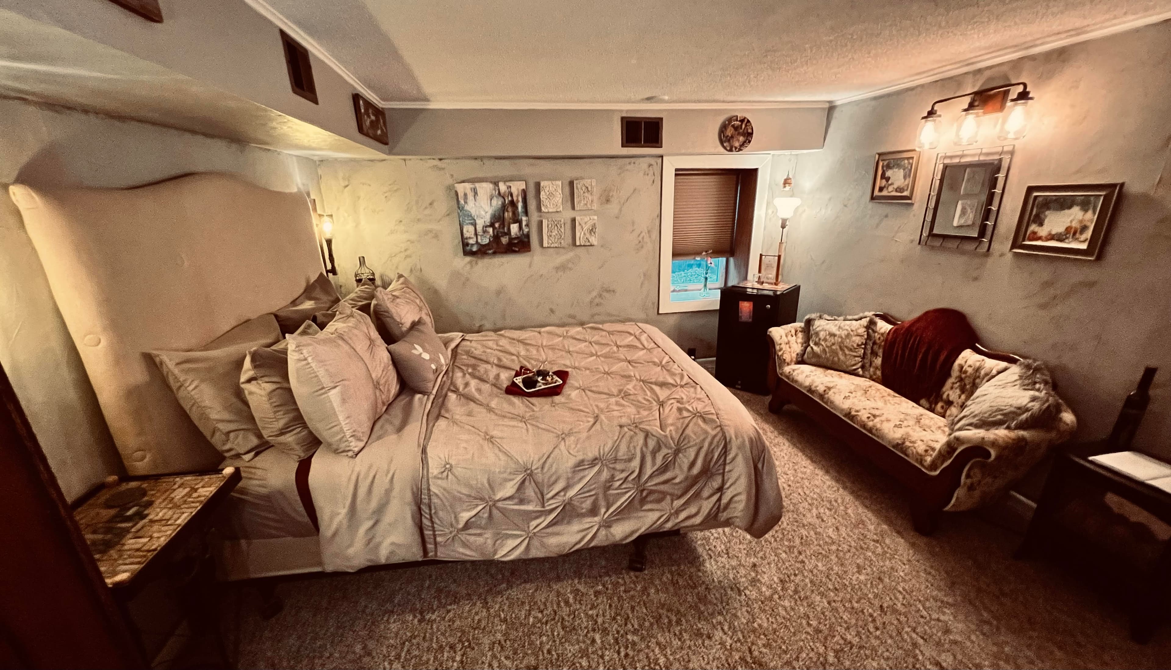 Inviting bedroom with a queen bed featuring a high upholstered headboard, sumptuous pillows, and a lovely antique floral settee.