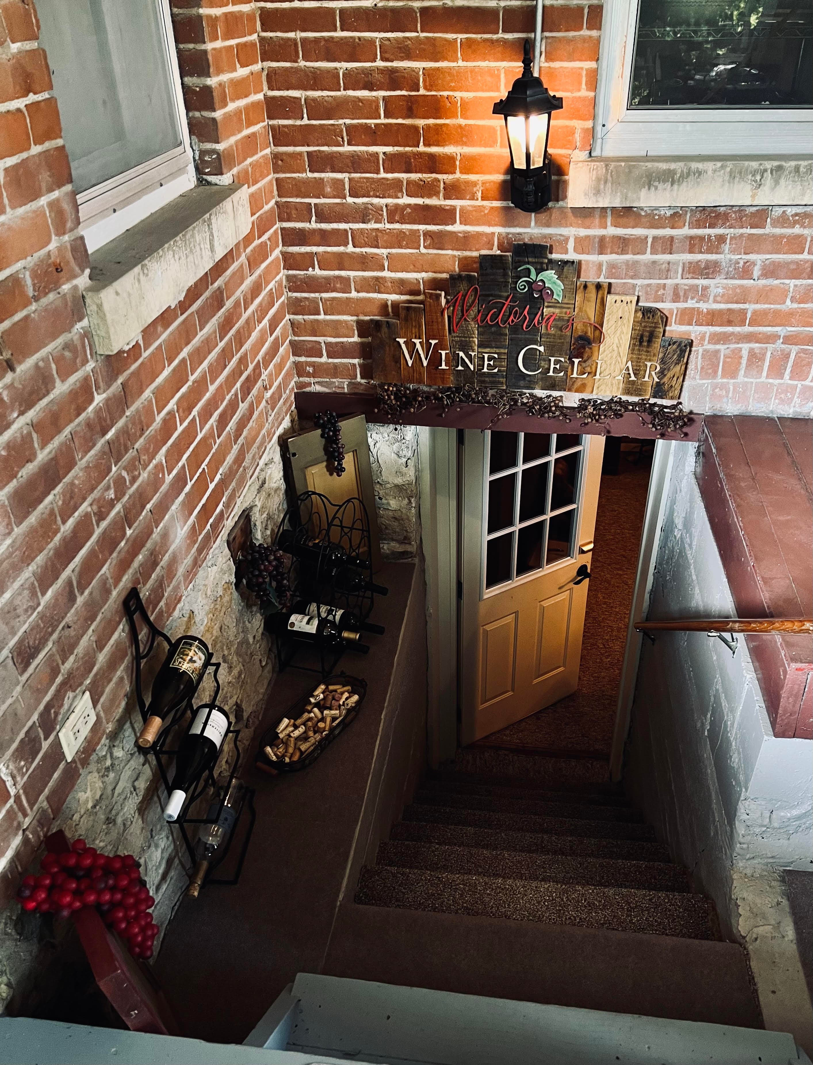 Exterior stairway of brick building leading down to private entrance to Victoria's Wine Cellar guestroom above the doorway hangs a painted wooden sign with Victoria's Wine Cellar written on it.