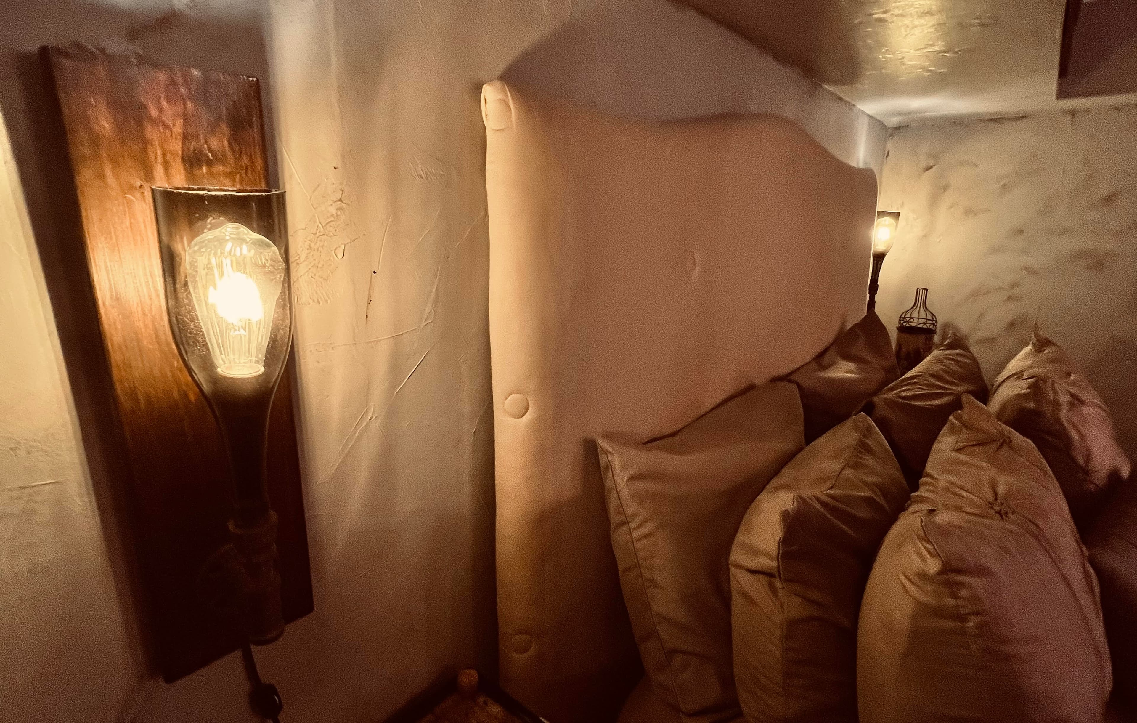 A vintage style wall sconce bathes the queen size bed's headboard and pillows in a soft glowing light.