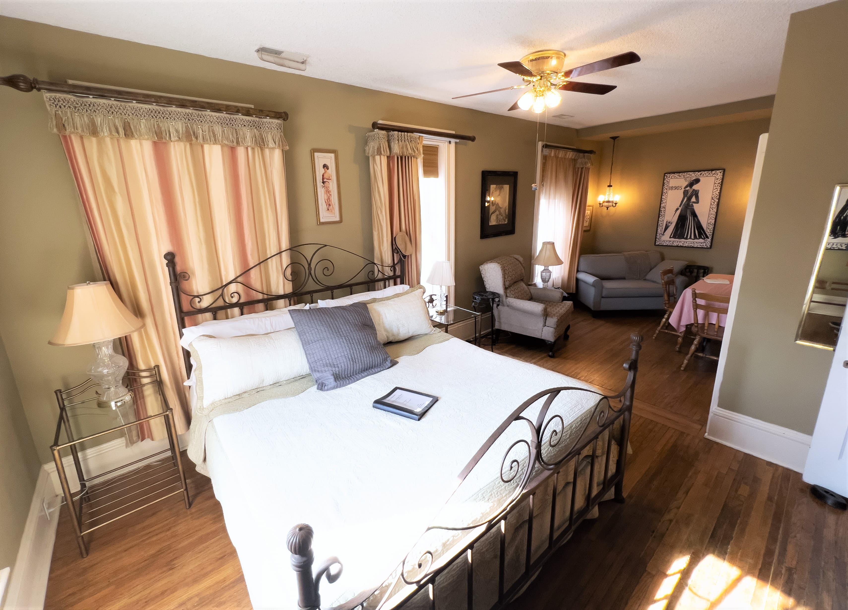 Romantic guest room with king iron bed, wood floors, a ceiling fan, and a cozy sitting area.