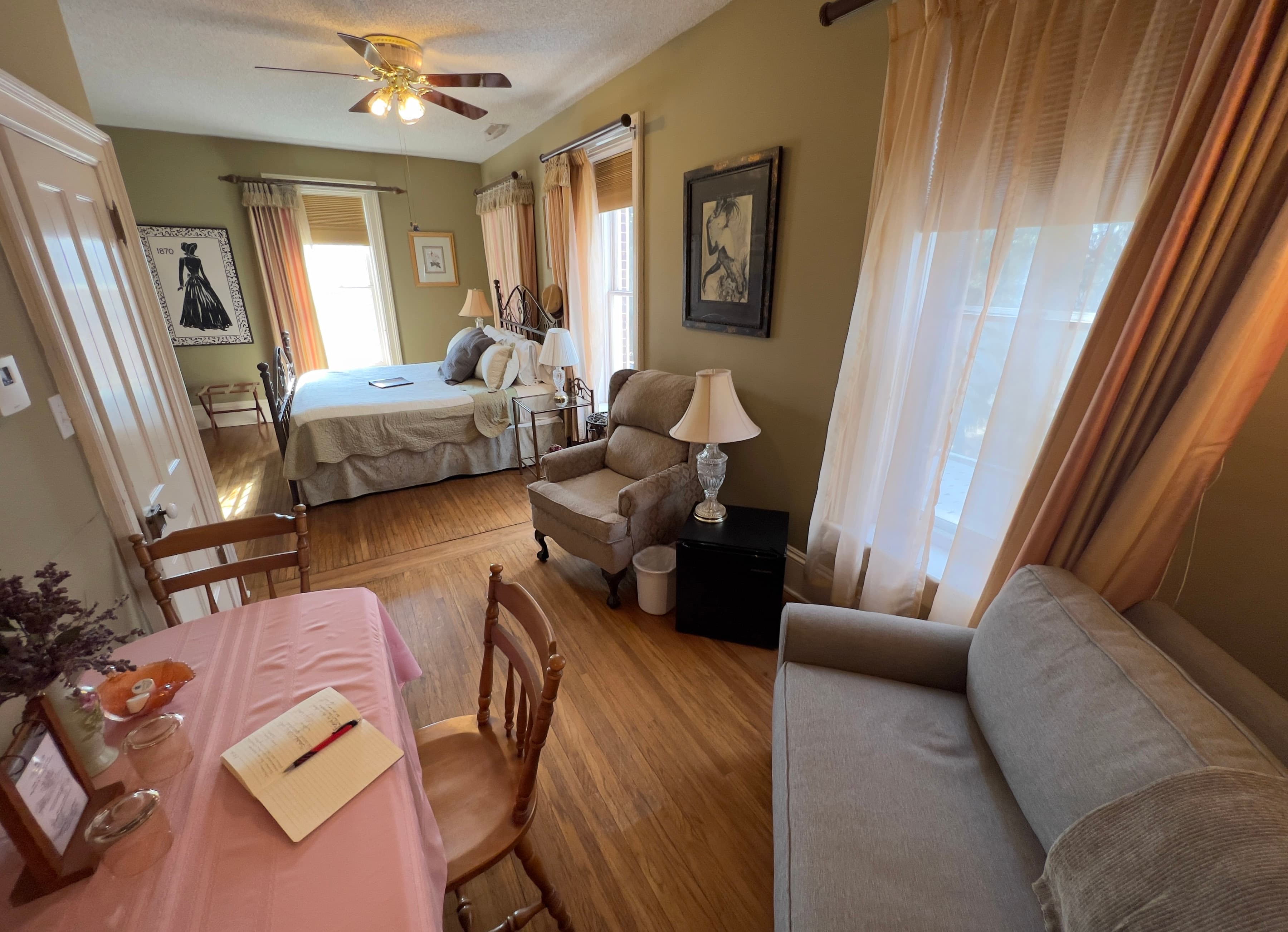 View of the guest room from the sitting nook with chair & a half, table and chairs, and large window with French silk curtains