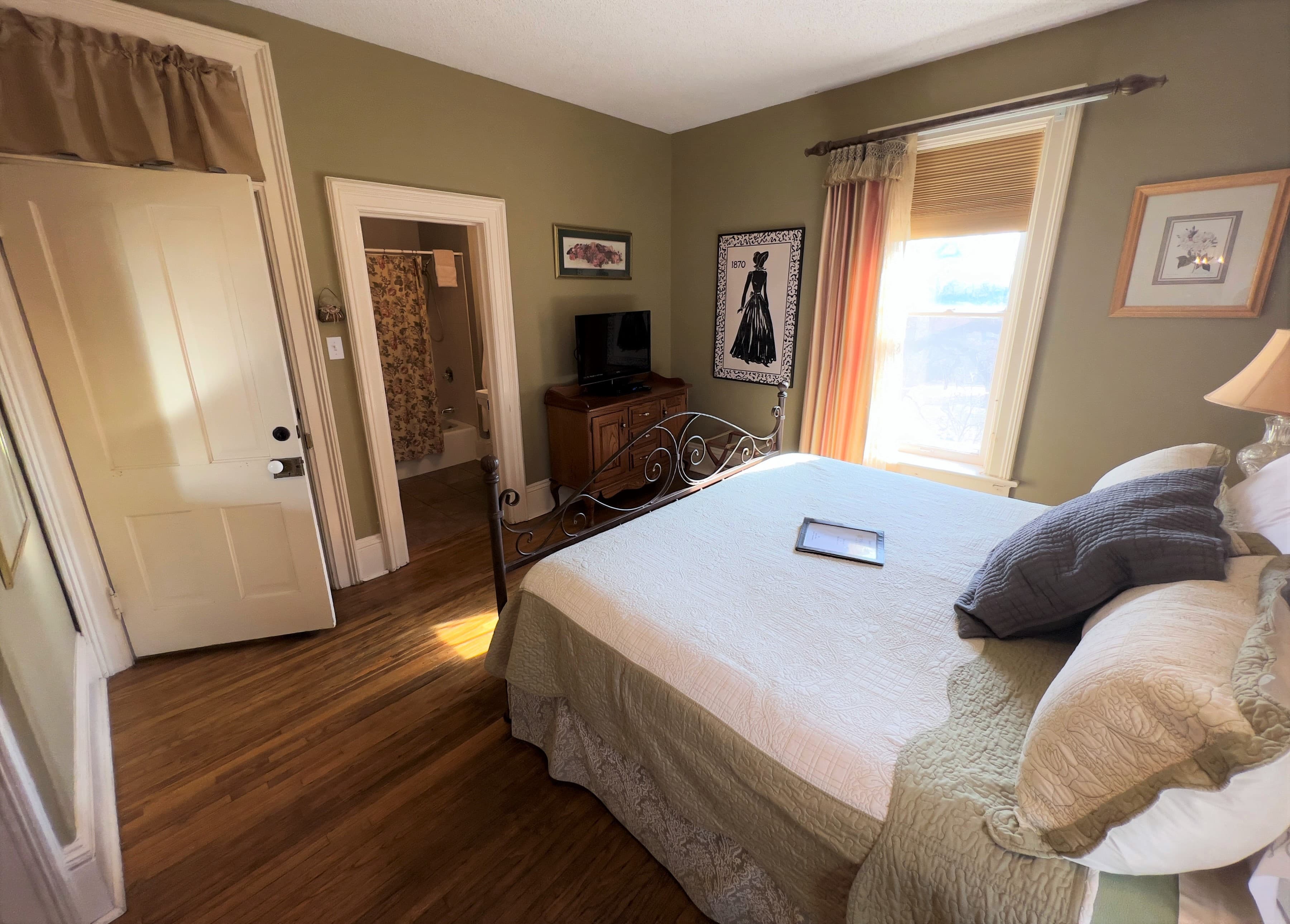 The sleeping area of the Rose Room features a king size iron bed and a large window with French silk curtains and room-darkening shades