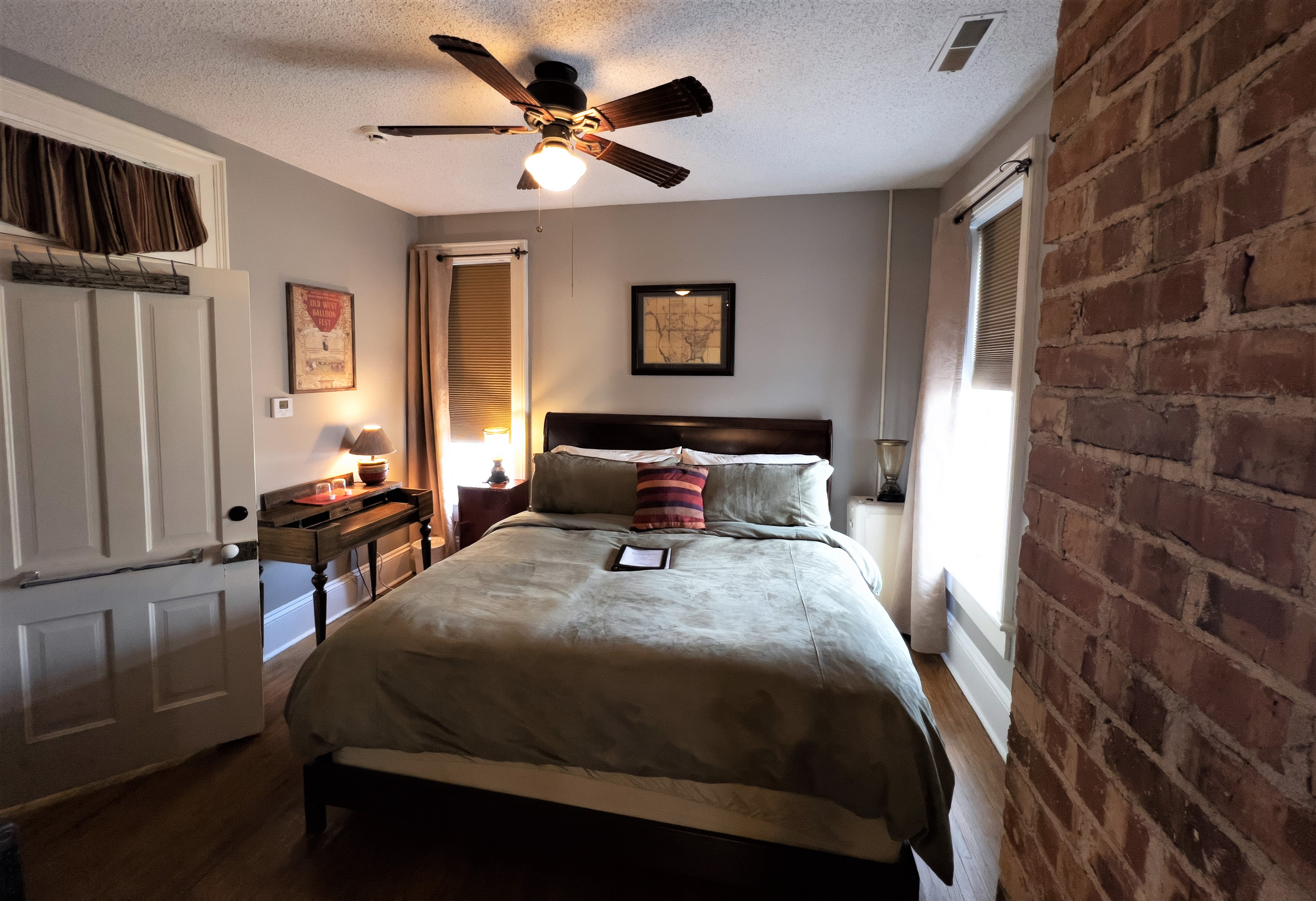 Warm, stately bedroom with king size sleigh bed, antique Missionary desk, and exposed brick chimney