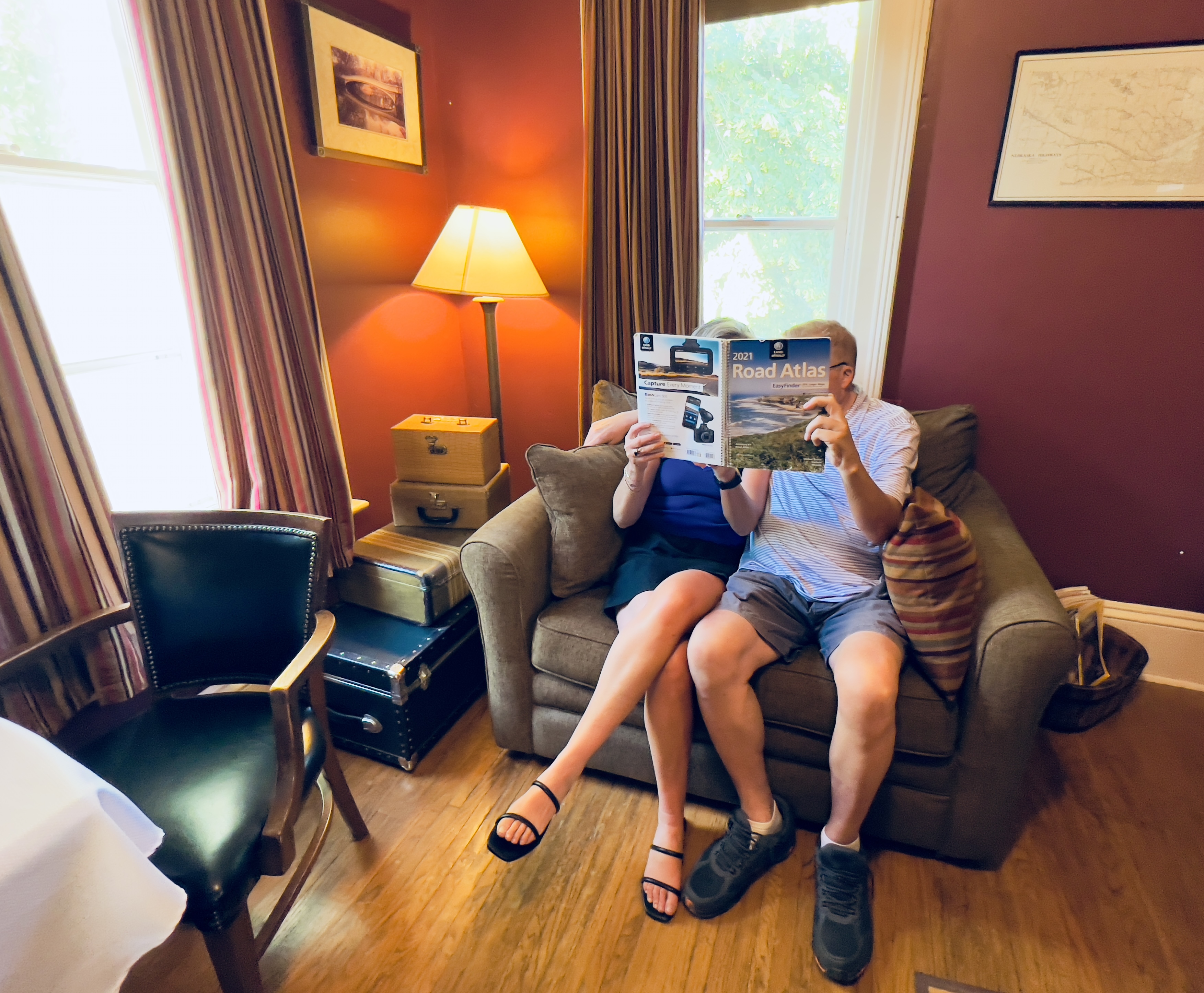 A couple sits on the oversized chair reading a magazine together by the light of a floor lamp.