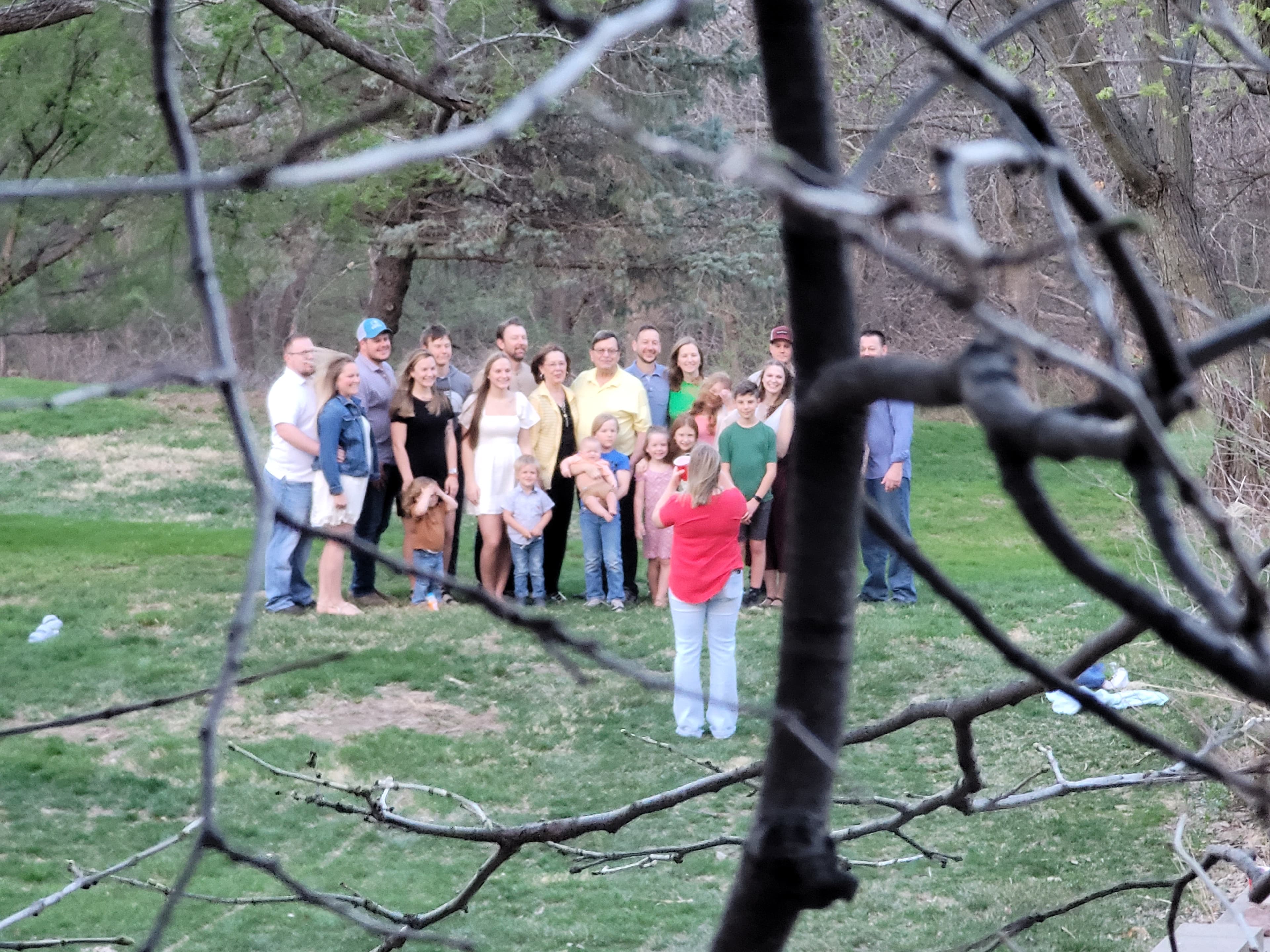 A multi-generational family posing for a photo outside on a green lawn near the treeline