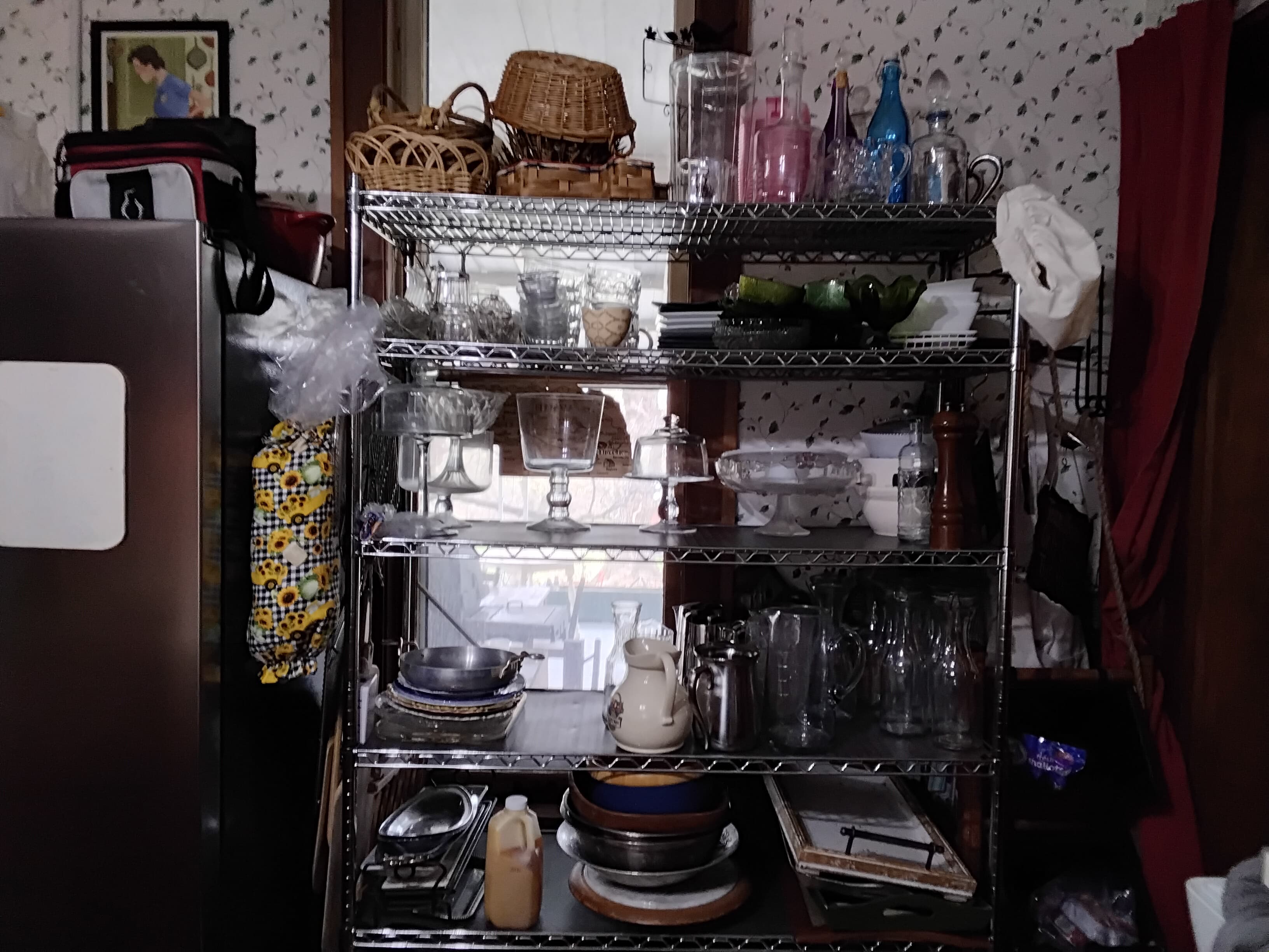 A shelf filled with various glassware, dishes, and kitchen items against a patterned wall.