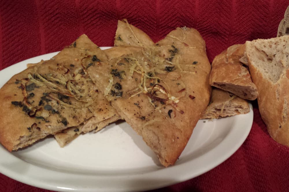 A plate of flatbread with herbs and sliced pieces alongside a loaf of rustic bread.