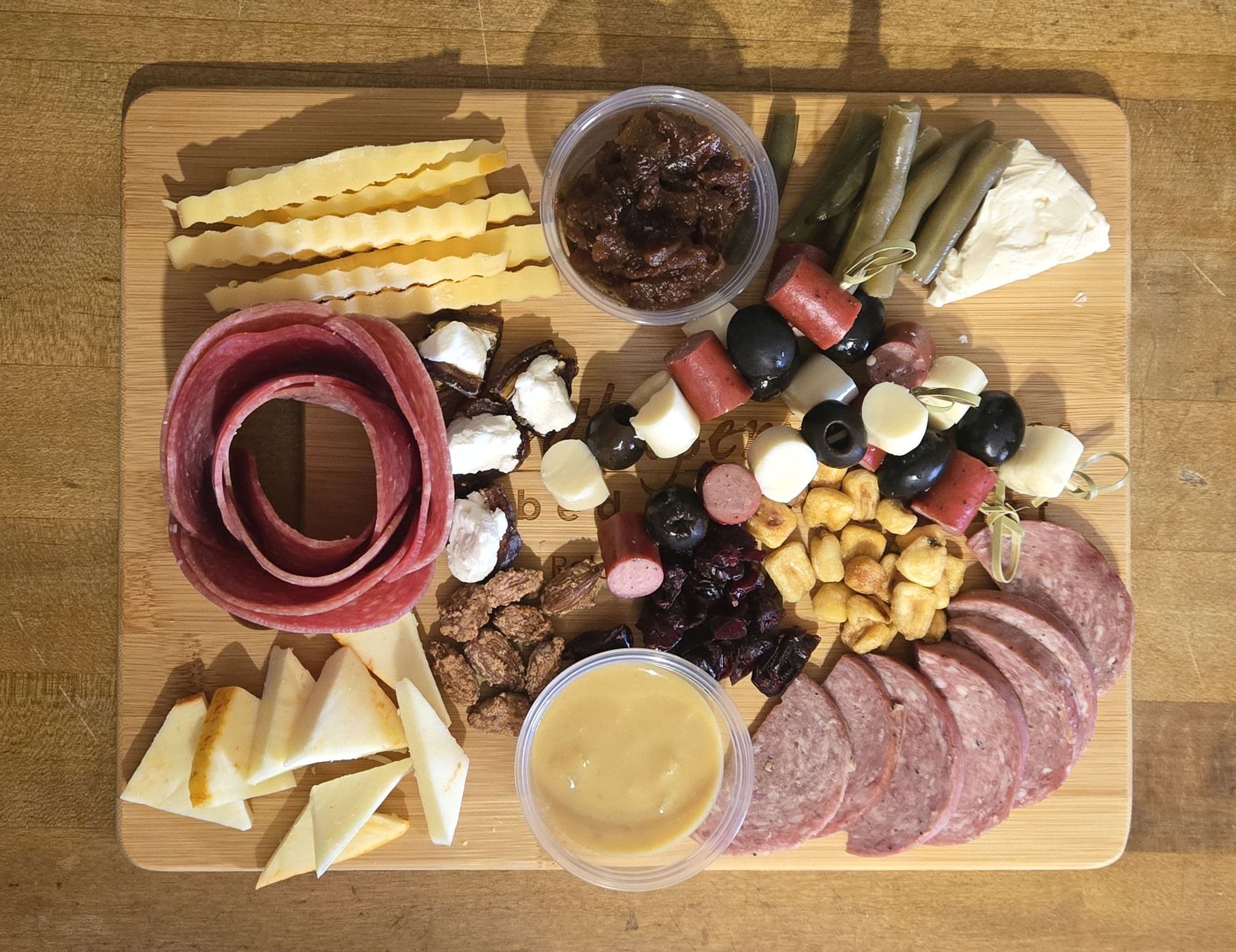A wooden board featuring an assortment of meats, cheeses, olives, nuts, and dips arranged for a charcuterie platter.