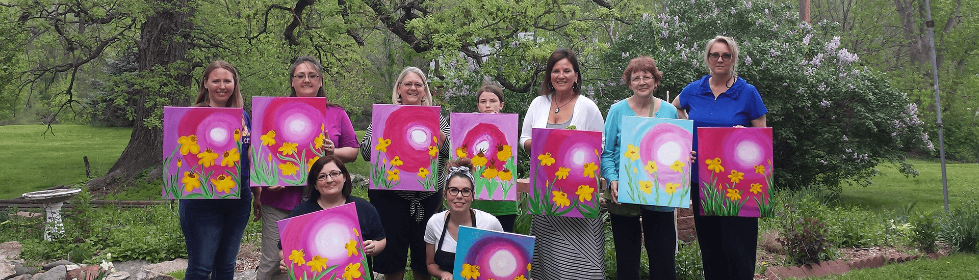 A group of women proudly display their colorful flower paintings outdoors.