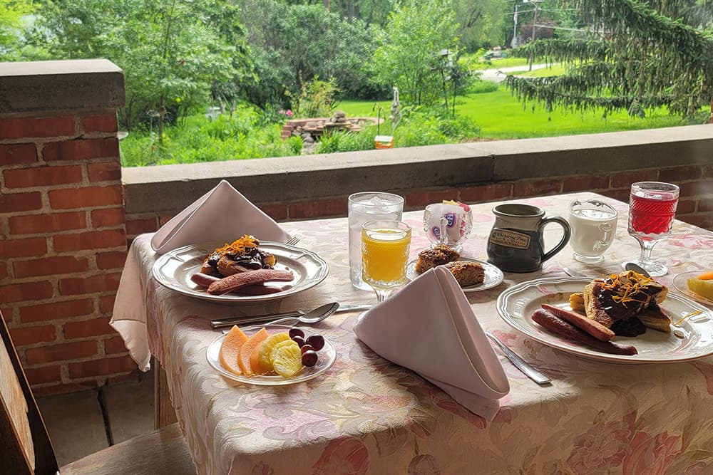 A beautifully set outdoor table with a variety of breakfast foods and drinks, surrounded by greenery.