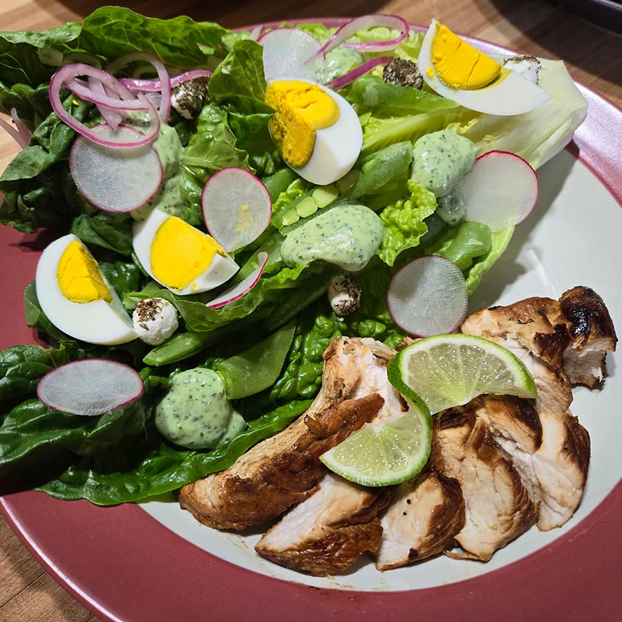 A vibrant salad with greens, sliced eggs, radishes, and grilled chicken garnished with lime.