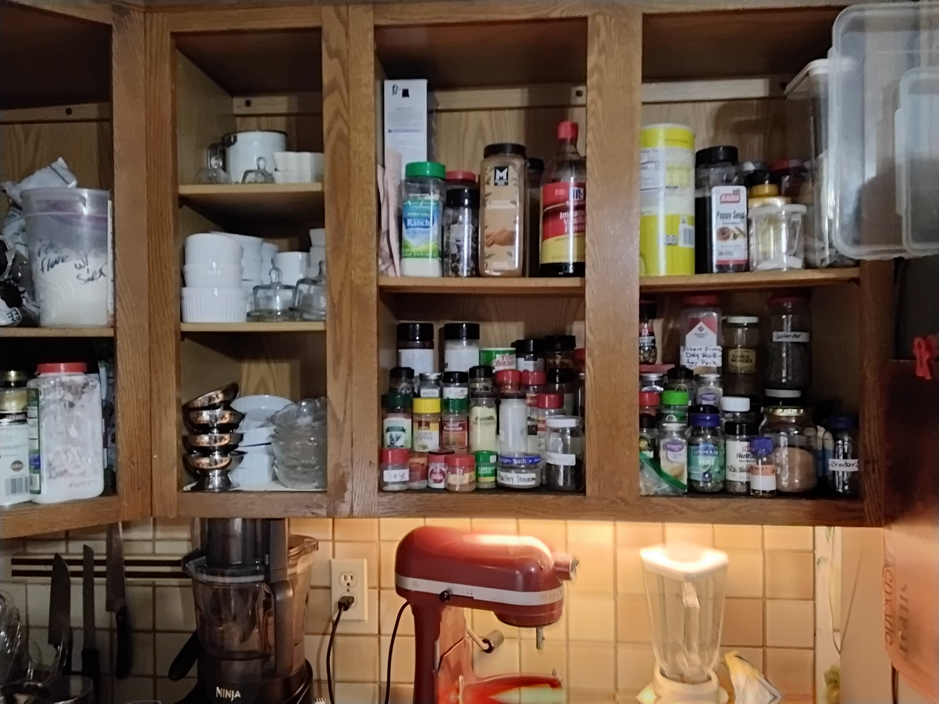 A cluttered kitchen cabinet filled with various spices, jars, and dishes.
