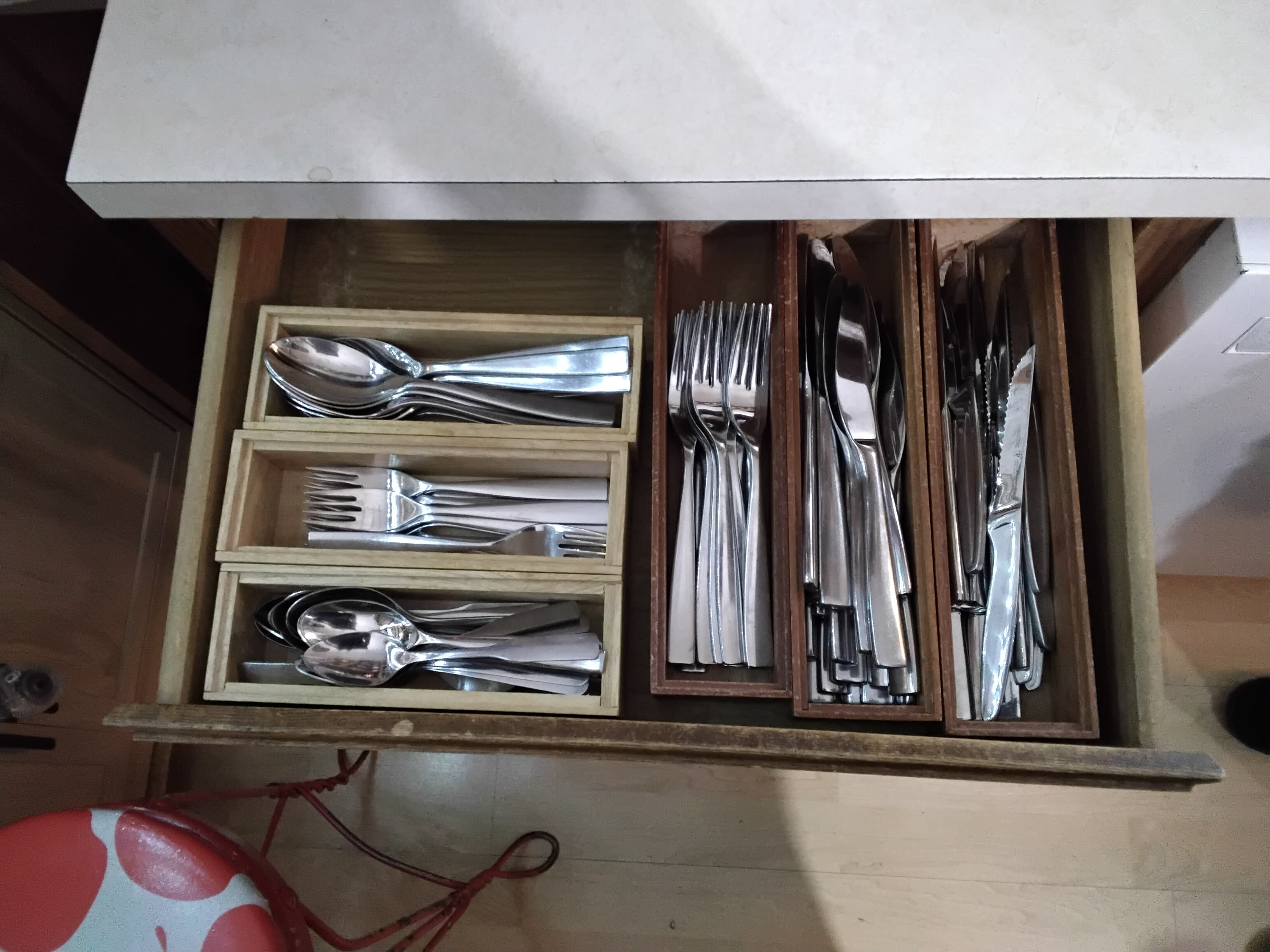 A wooden drawer organized with various utensils, including spoons, forks, and knives.