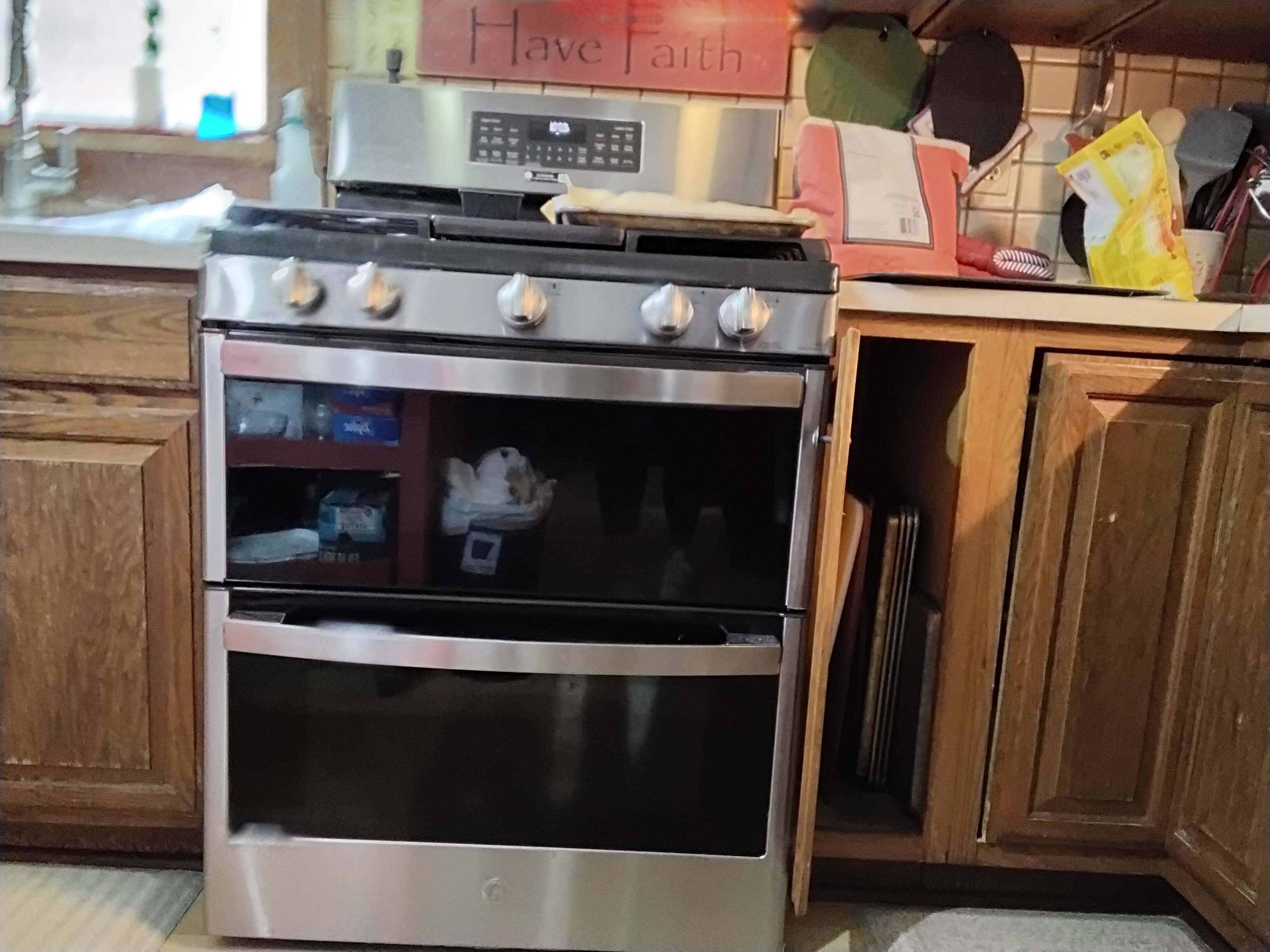 A stainless steel oven with a digital display, situated in a kitchen with wooden cabinetry.