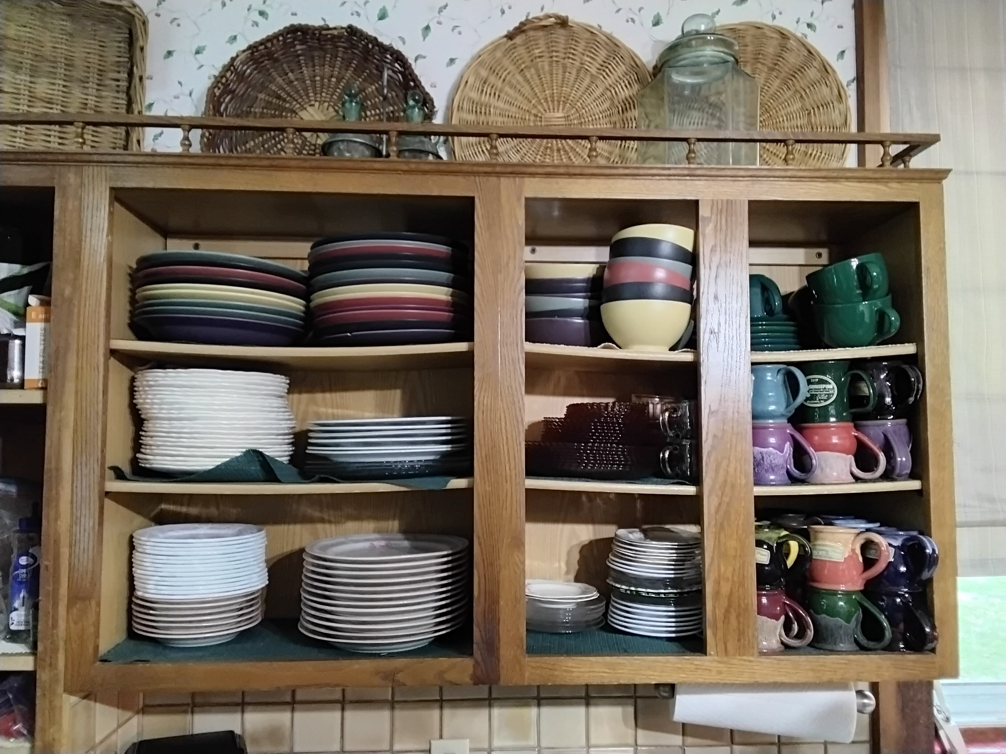 A wooden cabinet filled with various stacked plates, bowls, and mugs in different colors.