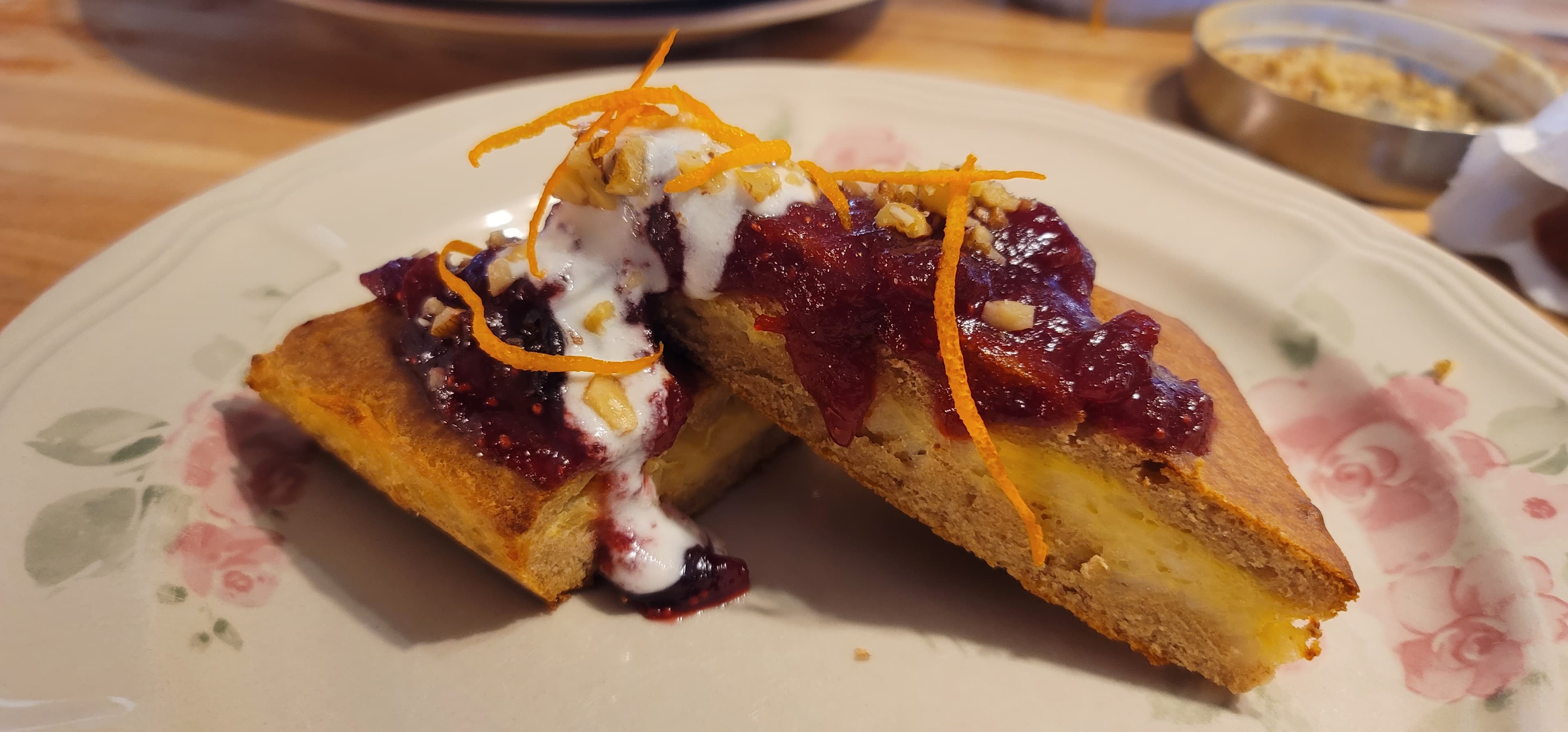 Two pieces of baked dessert topped with cranberry sauce, yogurt, and orange zest on a floral plate.