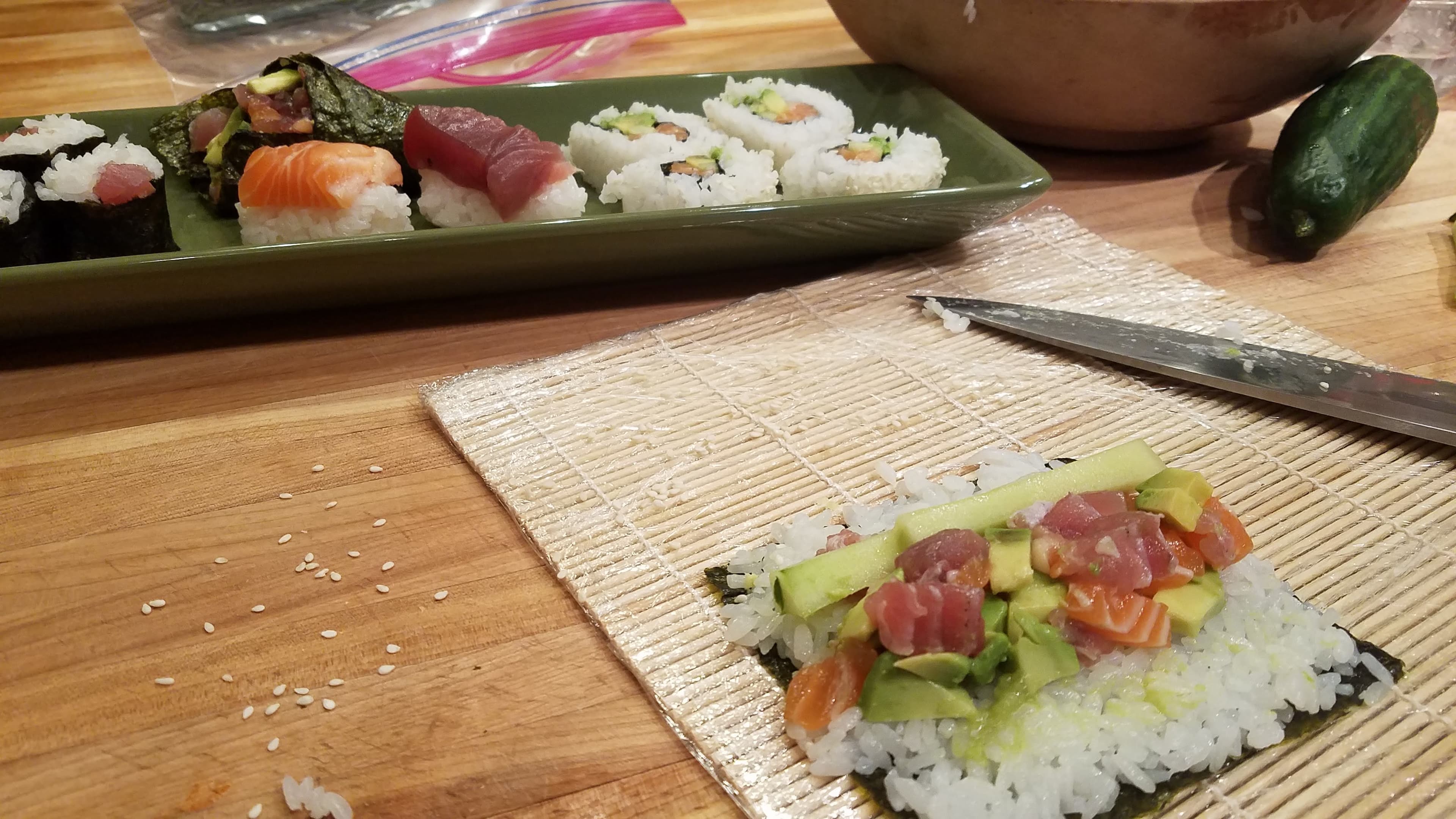 A sushi-making setup featuring a bamboo mat, sliced ingredients, and completed sushi rolls on a plate.