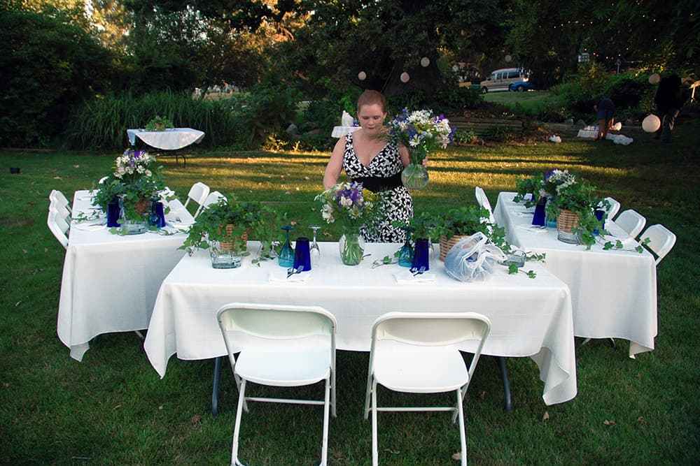 A woman arranges flowers on elegantly set tables in a garden.