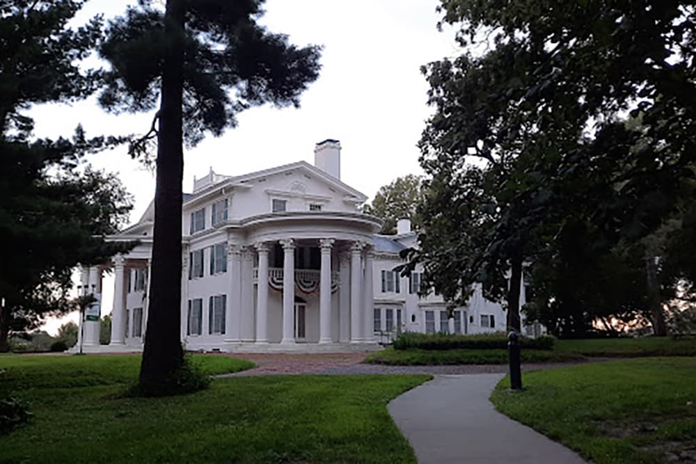 A stately white mansion with columns set within a lush green landscape.