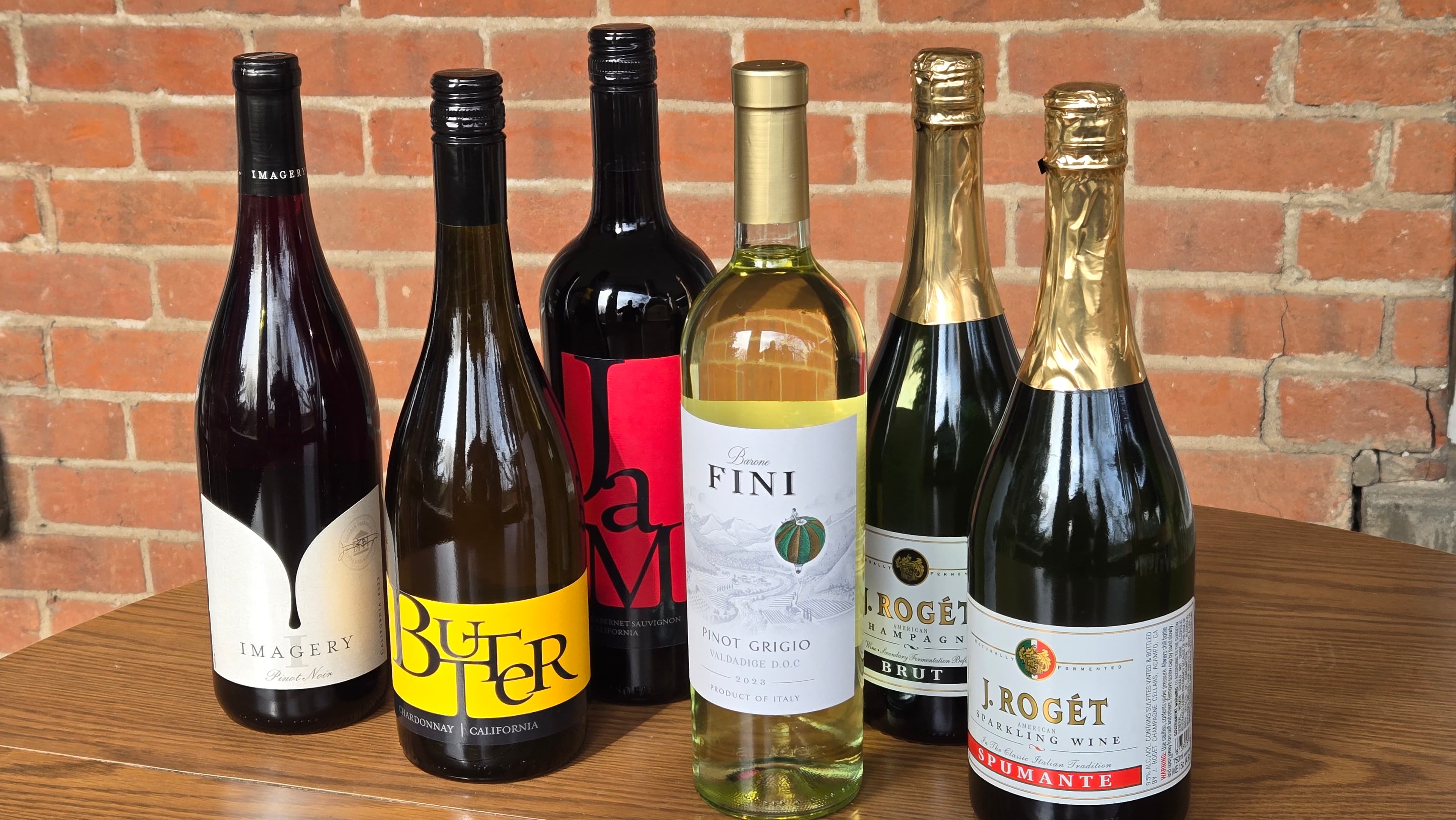 A selection of six wine bottles displayed on a wooden table against a brick wall. A selection of six wine bottles displayed on a wooden table against a brick wall.