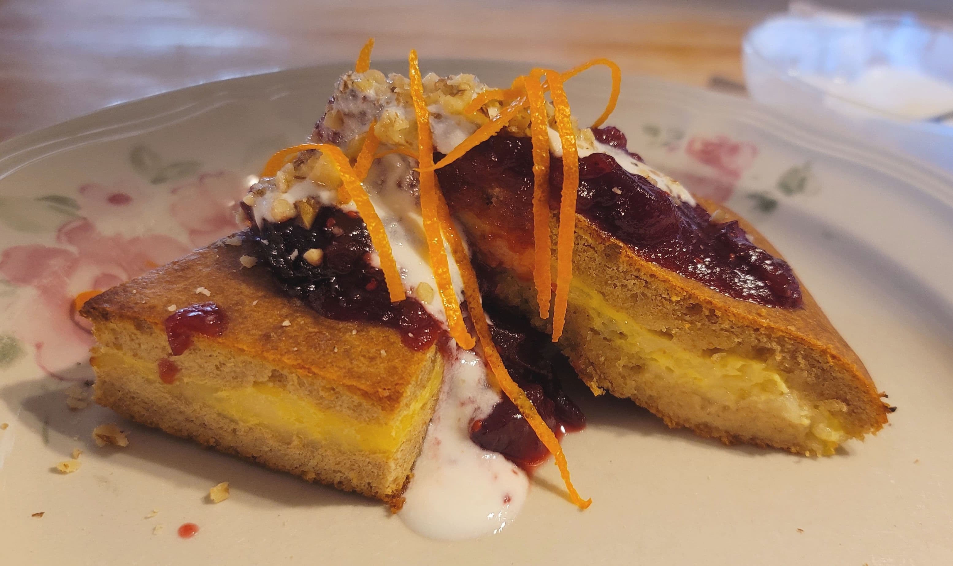 A slice of layered dessert topped with fruit preserves, cream, and orange zest on a decorative plate. A slice of layered dessert topped with fruit preserves, cream, and orange zest on a decorative plate.