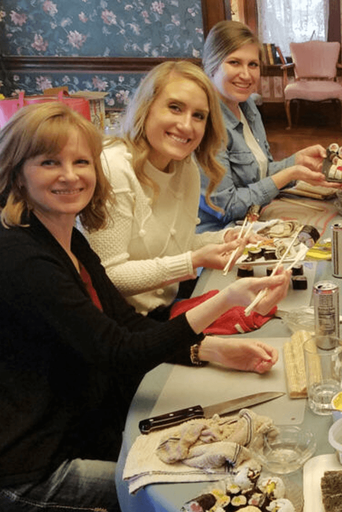Three women sitting at table with chopsticks eating sushi