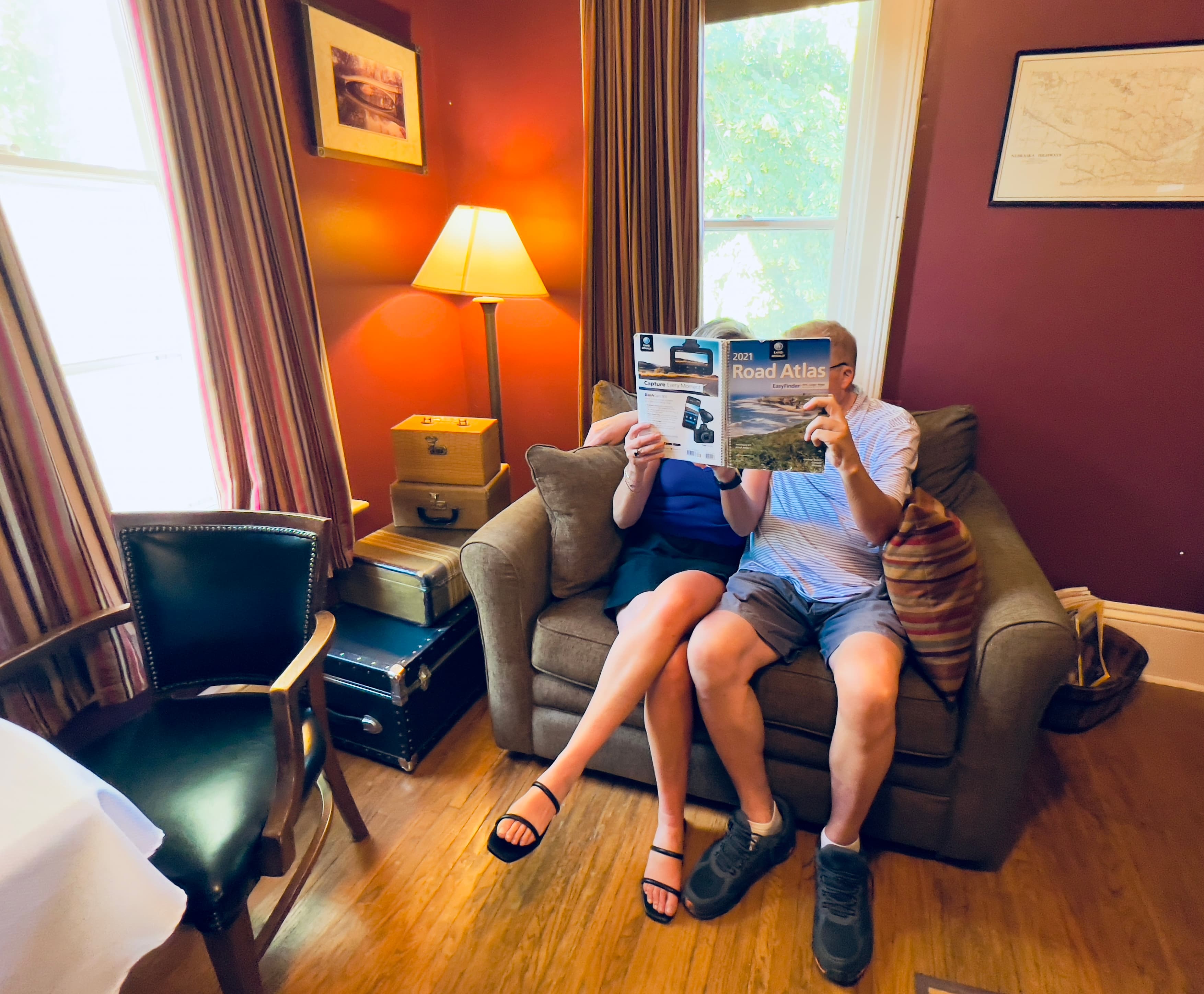 A couple sits on the oversized chair reading a magazine together by the light of a floor lamp.