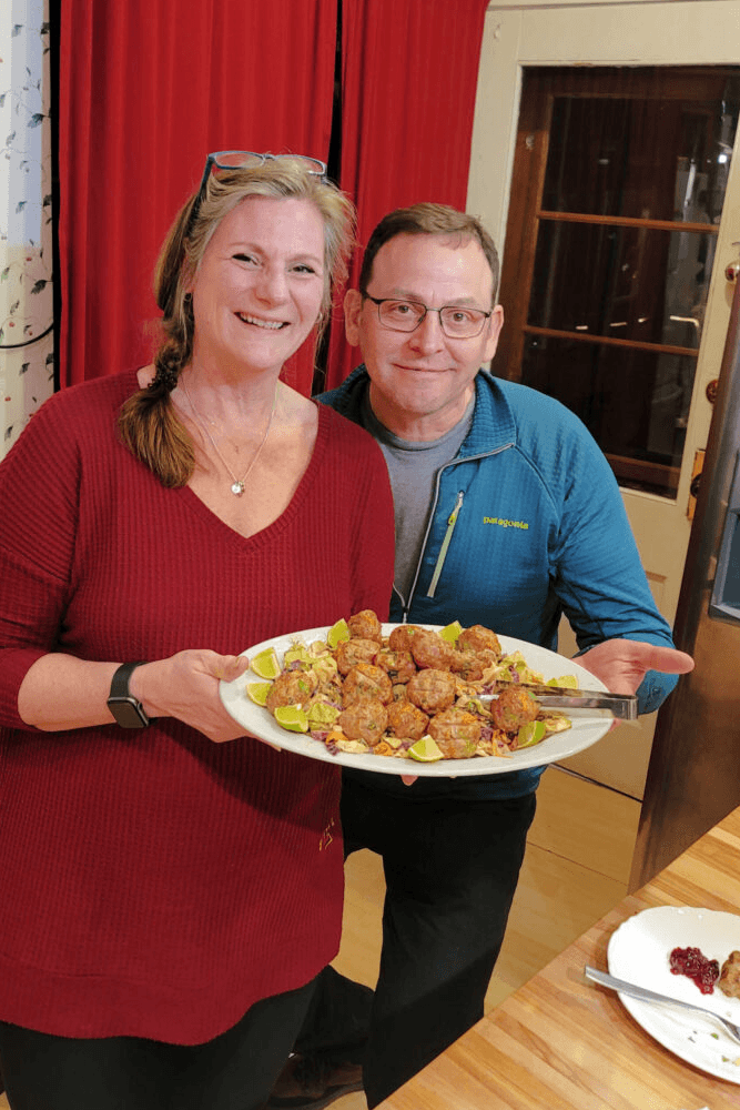 Man and woman in kitchen holding a large plate of food