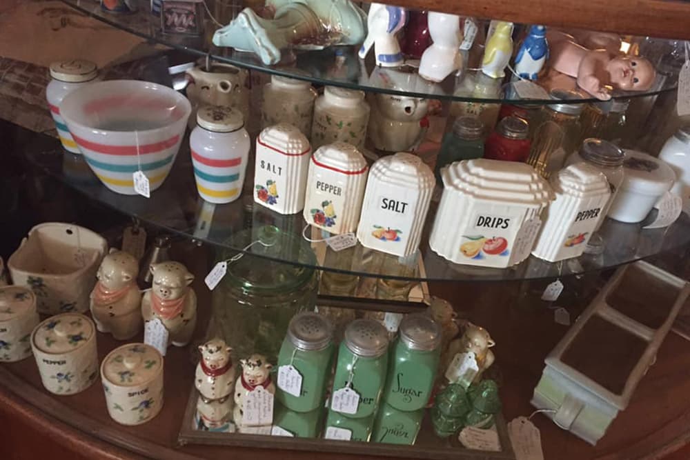 A display case filled with various vintage kitchenware, including bowls, salt and pepper shakers, and small decorative figurines.