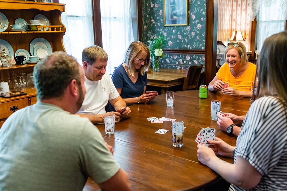 A group of people playing cards at a dining room table.