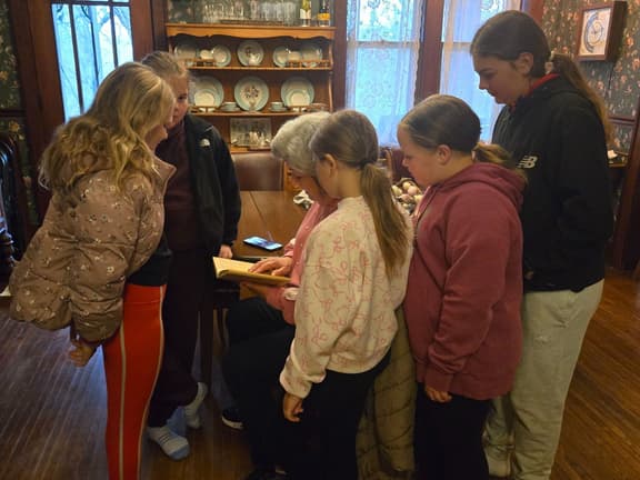 Grandmother and granddaughters gathered around a Whispering Pines guest journal, reading an entry their family left six years earlier.