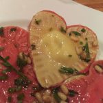 Heart-shaped ravioli with red beet pasta on one side and regular pasta on the other. Sprinkled with pine nuts and browned sage.