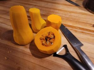 Three butternut squash just peeled with peeler and chef's knife next to them.
