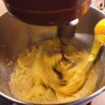 Adding an egg to a mixer in motion with the choux dough in it
