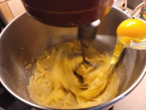Adding an egg to a mixer in motion with the choux dough in it