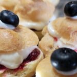 Mini Creampuffs with a smear of red raspberry jam, filled with white cream cheese custard topped with a blueberry on silver tray
