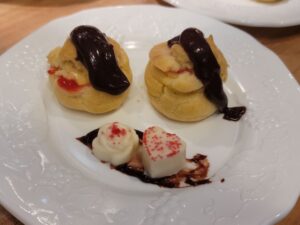 Vanilla custard filled cream puffs with lemon raspberry glaze and topped with hot fudge.